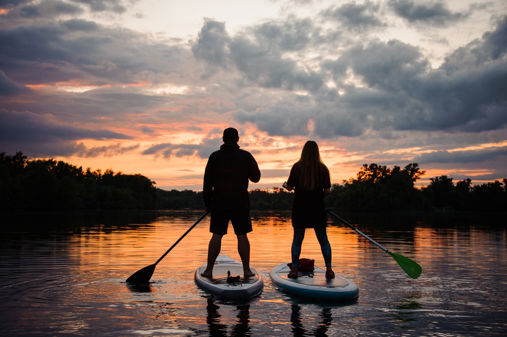 couple enjoying a sunset paddle board, a great way to wind down a day of fun on the water during Midwest summer getaways