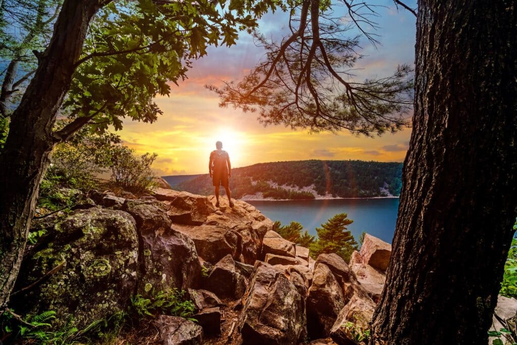 A silhouette of a man looking out into the sunset over Devils Lake State Park from a hiking viewpoint in Baraboo, Wisconsin